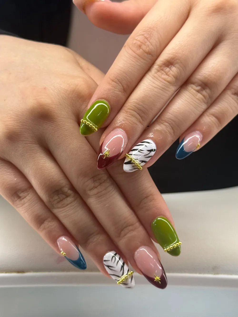 Almond nails in olive green, burgundy French tips and zebra print with gold bead details
